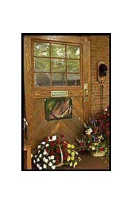 A photo and flowers, including roses, black-eyed susans, and carnations, adorn the stall door where Seattle Slew resided.